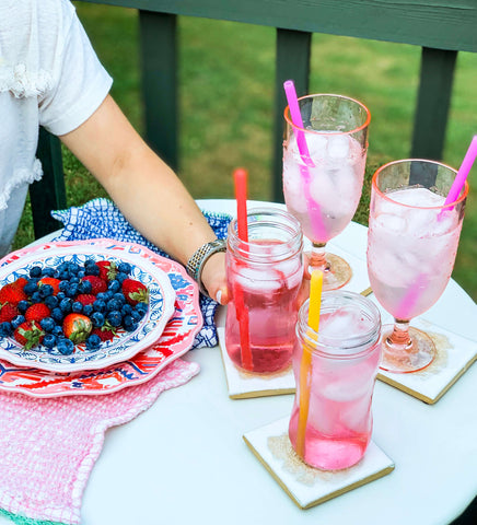 A ceramic bowl sitting on a table. Next to it there are four glasses filled with a pink bevarage. Each glass has a pink reusable silicone straw in it. 