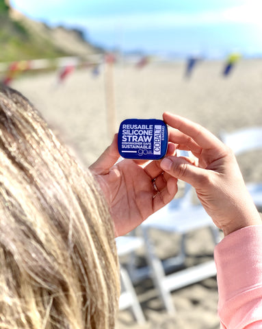 A person at the beach holding a travel tin with a reusable silicone straw in it