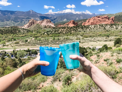 Two people holding reusable silicone cups with a background of red canyons and trees 