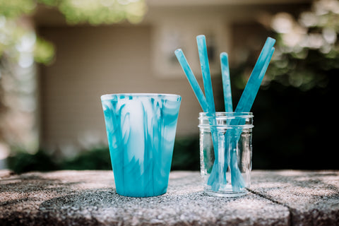 A reusable silicone cup sitting next to a glass jar filled with reusable silicone straws