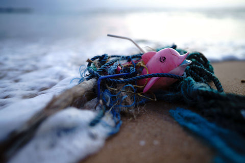 An old fishing net on the shore of a beach with a plastic dolphin entangled on it. 