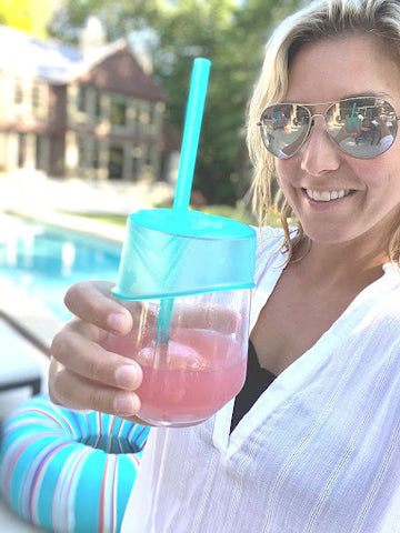 Woman holding a wine glass using a stretchy silicone lid. She's sitting by the pool on a bright, sunny day. 