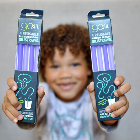 A child holding two packs of reusable silicone straws in front on him