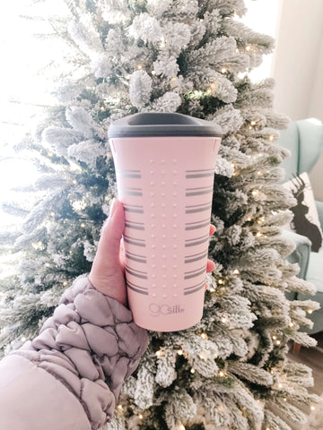 A person holding a pink Reusable Silicone Cup in front of a white Christmas tree