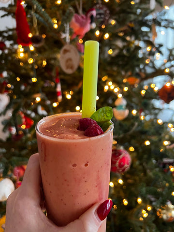 A women's hand holding a glass filled with a berry smoothie. In it is a extra-wide reusable silicone straw.